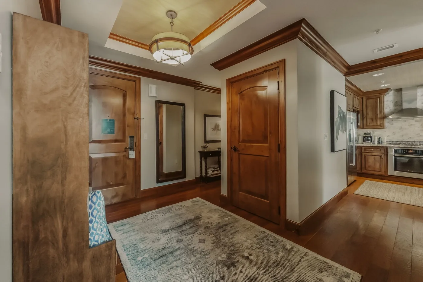 An entryway with wooden doors, a patterned rug, and a view into the kitchen.