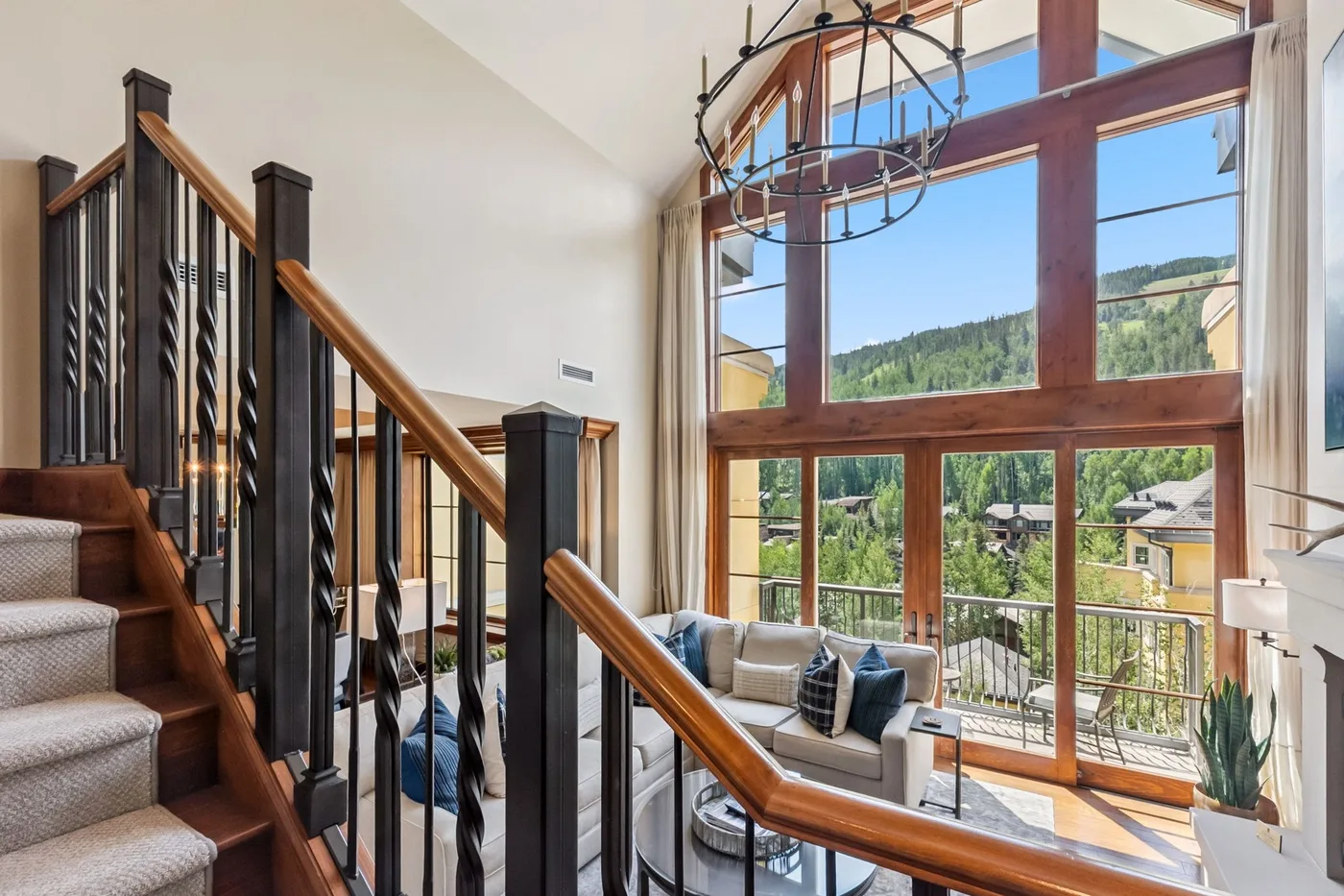 A living room with seating beside tall windows overlooking a wooded hillside.