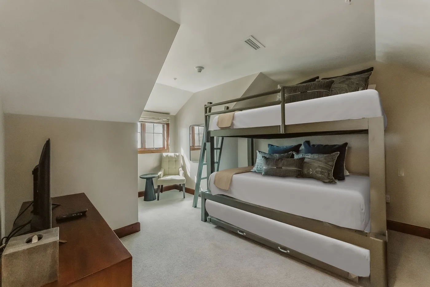 A bedroom with a bunk bed, a television, and a small seating area by the window.