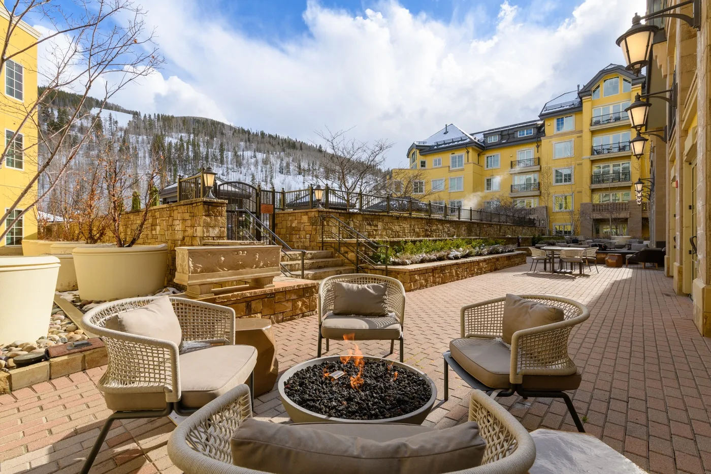 A paved outdoor courtyard with patio seating and yellow buildings around it.