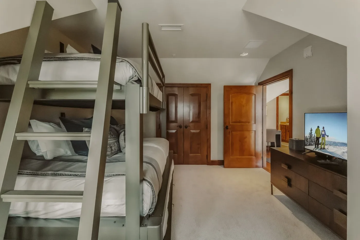A bedroom with bunk beds, wooden doors, and a television on a dresser.