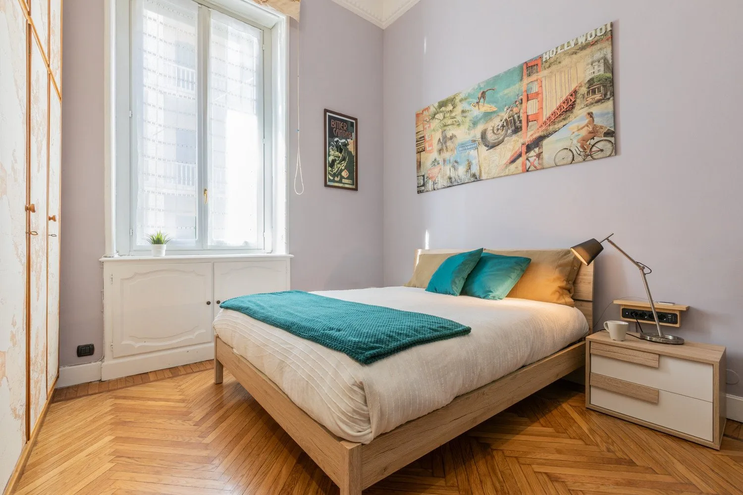 Un dormitorio con una cama vestida de blanco y turquesa junto a una ventana grande.