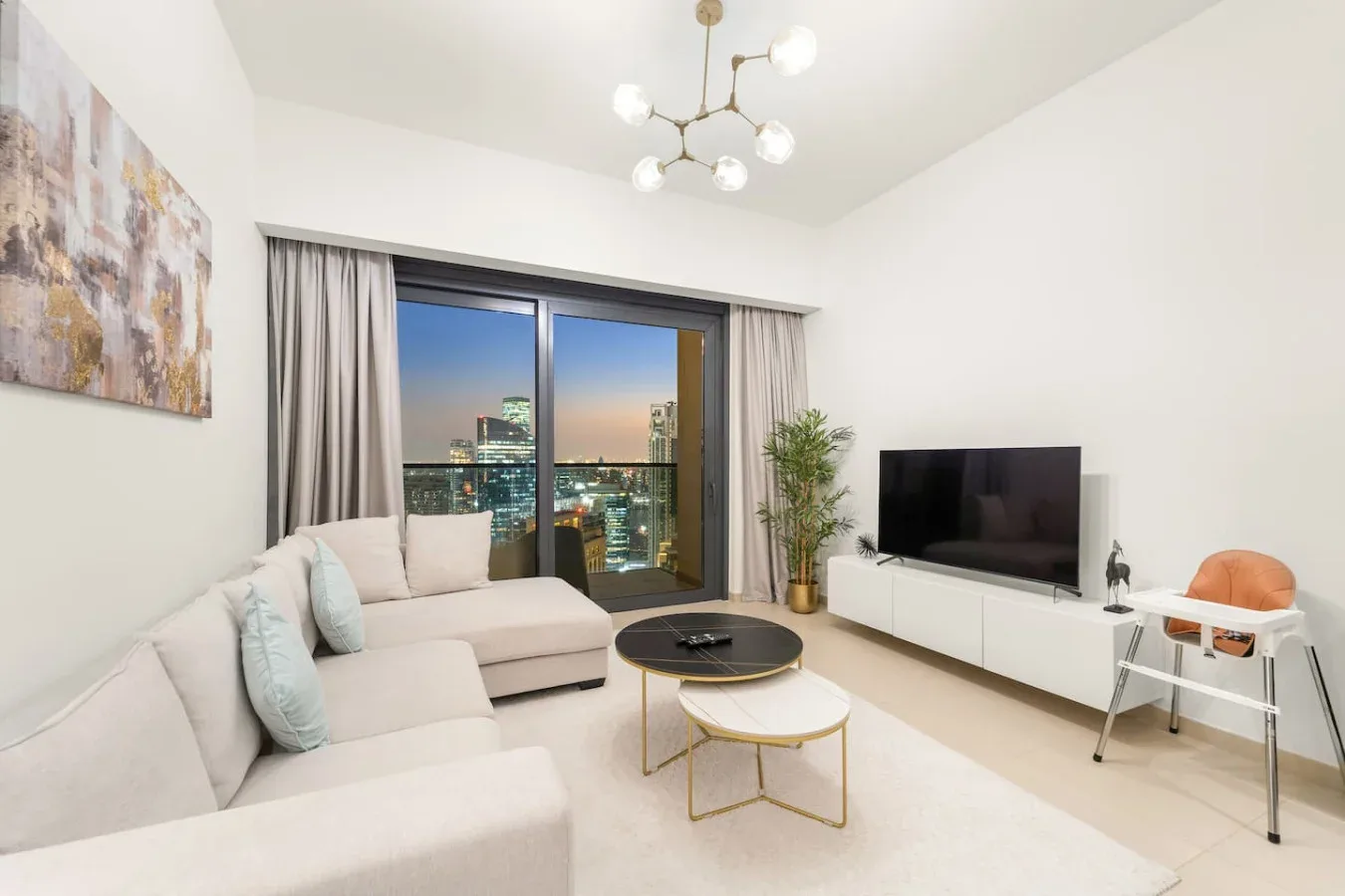 Una sala luminosa con asientos, un televisor y grandes ventanas con vistas a las luces de la ciudad.