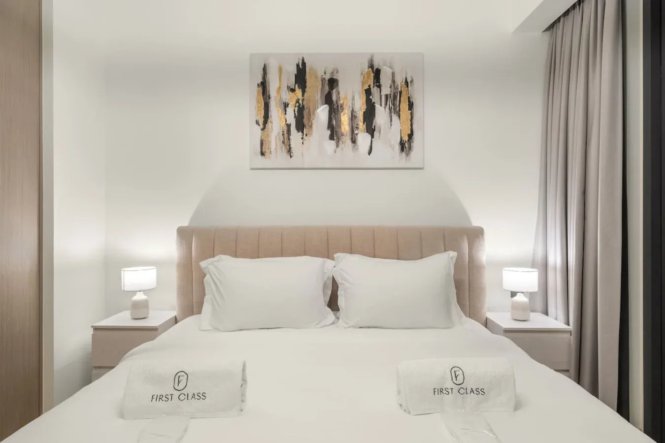 Un dormitorio con una cama tendida, mesitas de noche y arte abstracto en la pared.