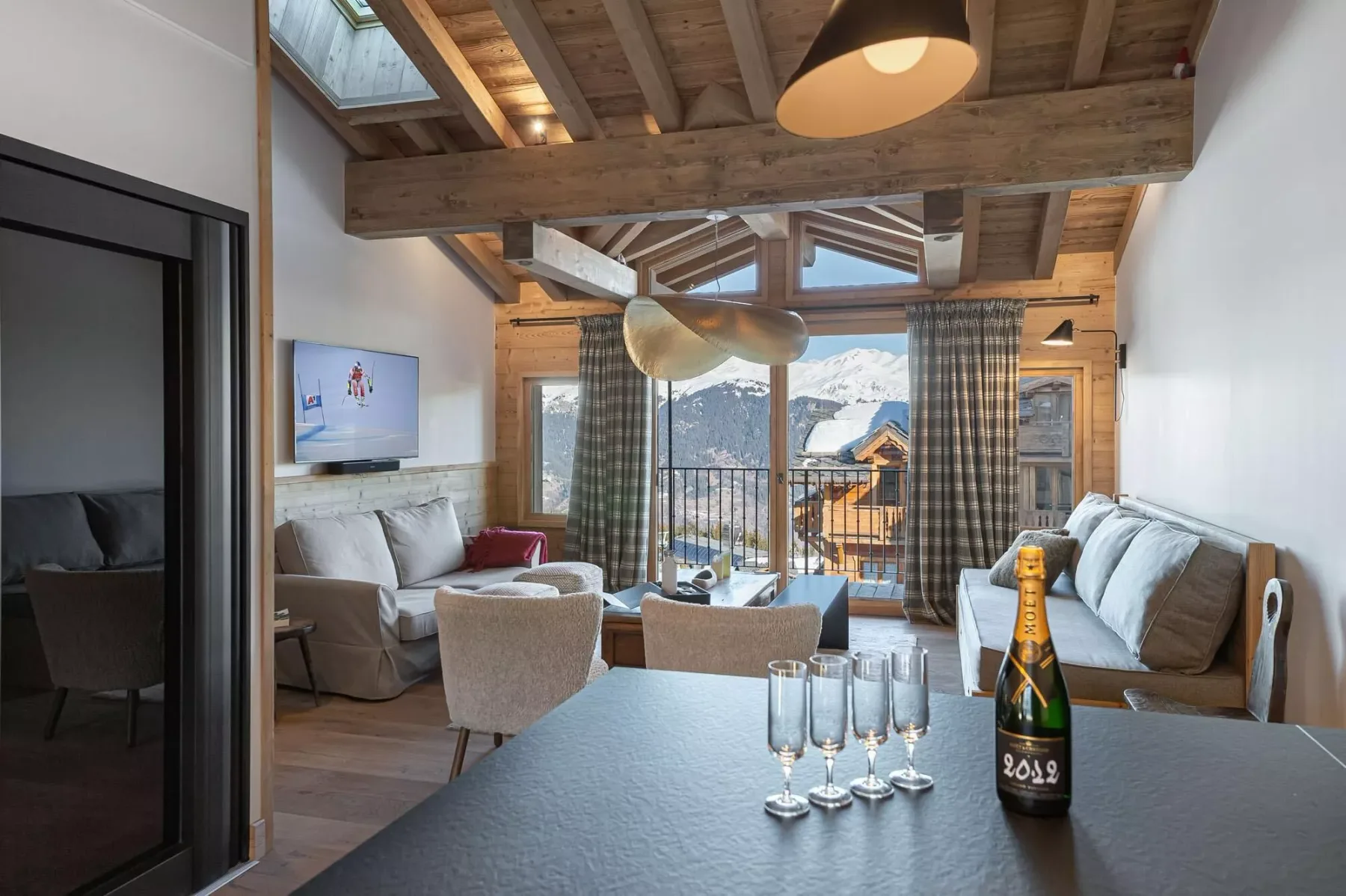 A wood-beamed living room with seating, a table, and mountain views through the windows.