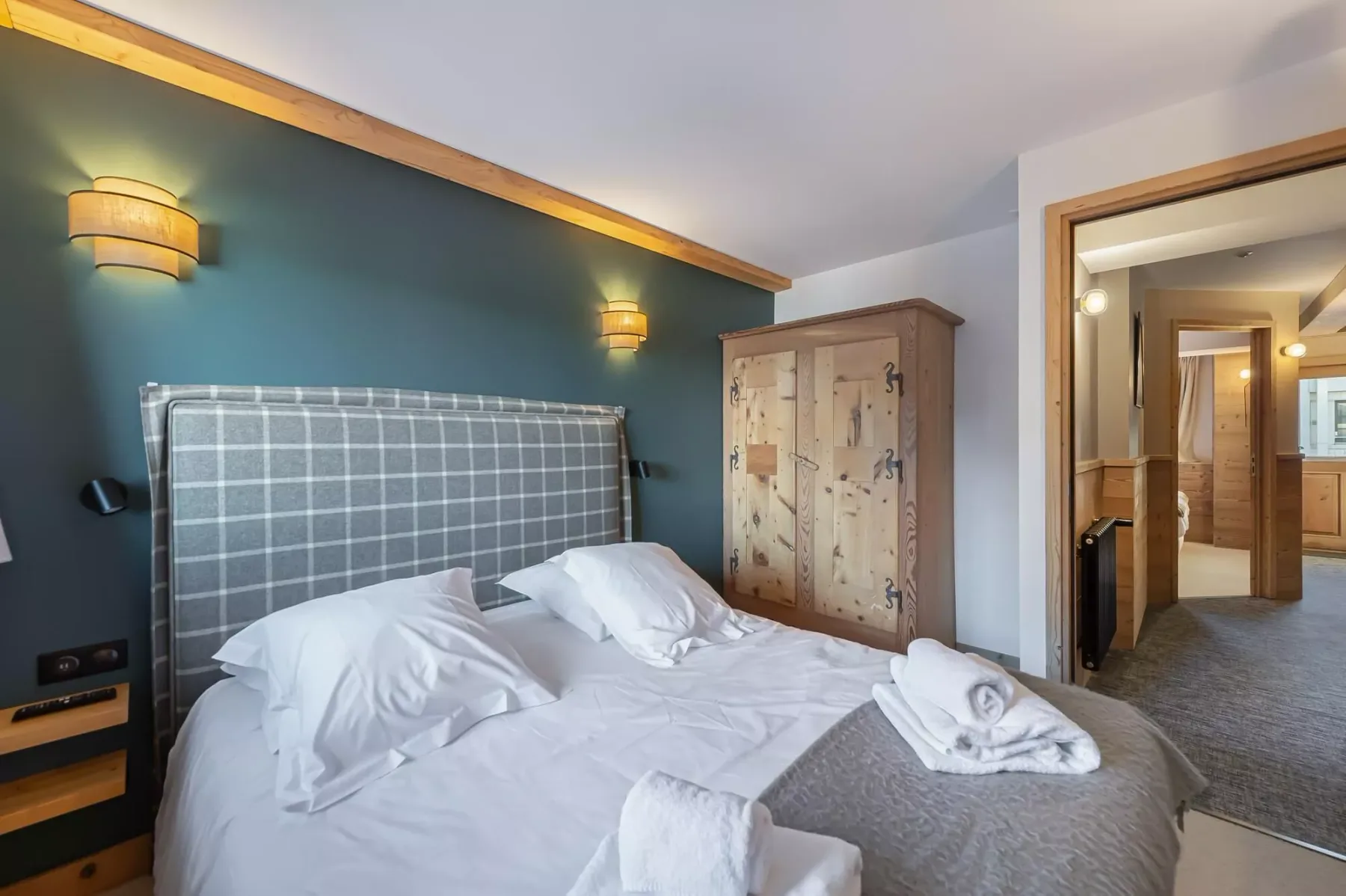 A bedroom with a large bed and a wooden wardrobe beside the open doorway.
