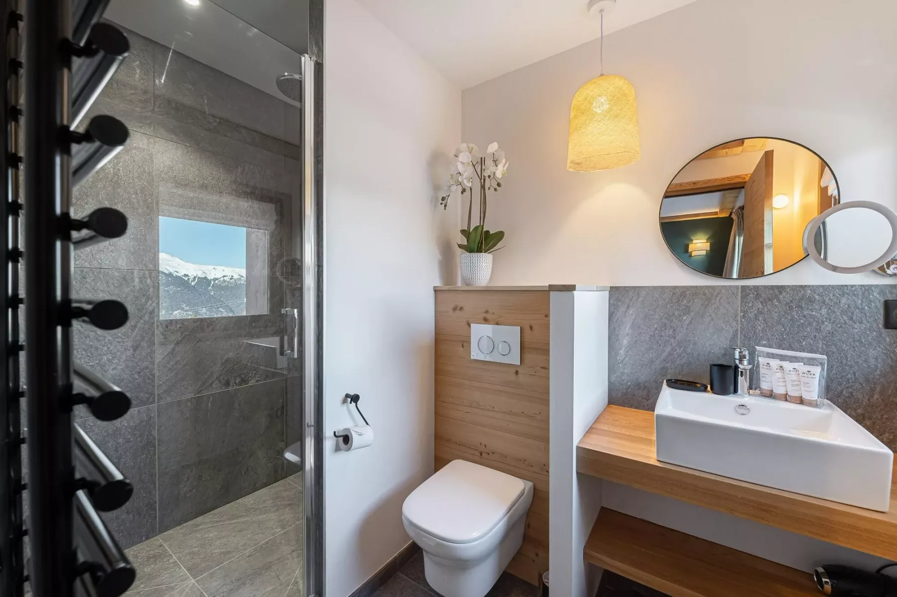 A bright bathroom with a glass shower, toilet, and wood vanity.