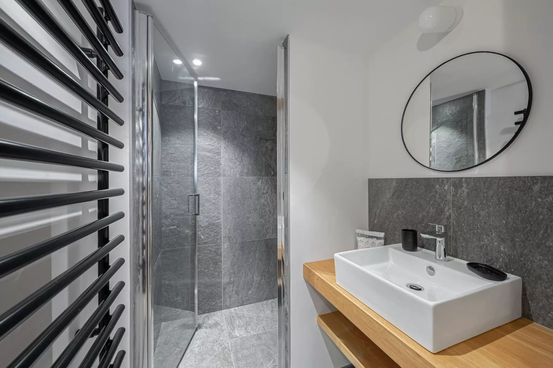 A modern bathroom with a glass shower and a white basin on a wooden counter.