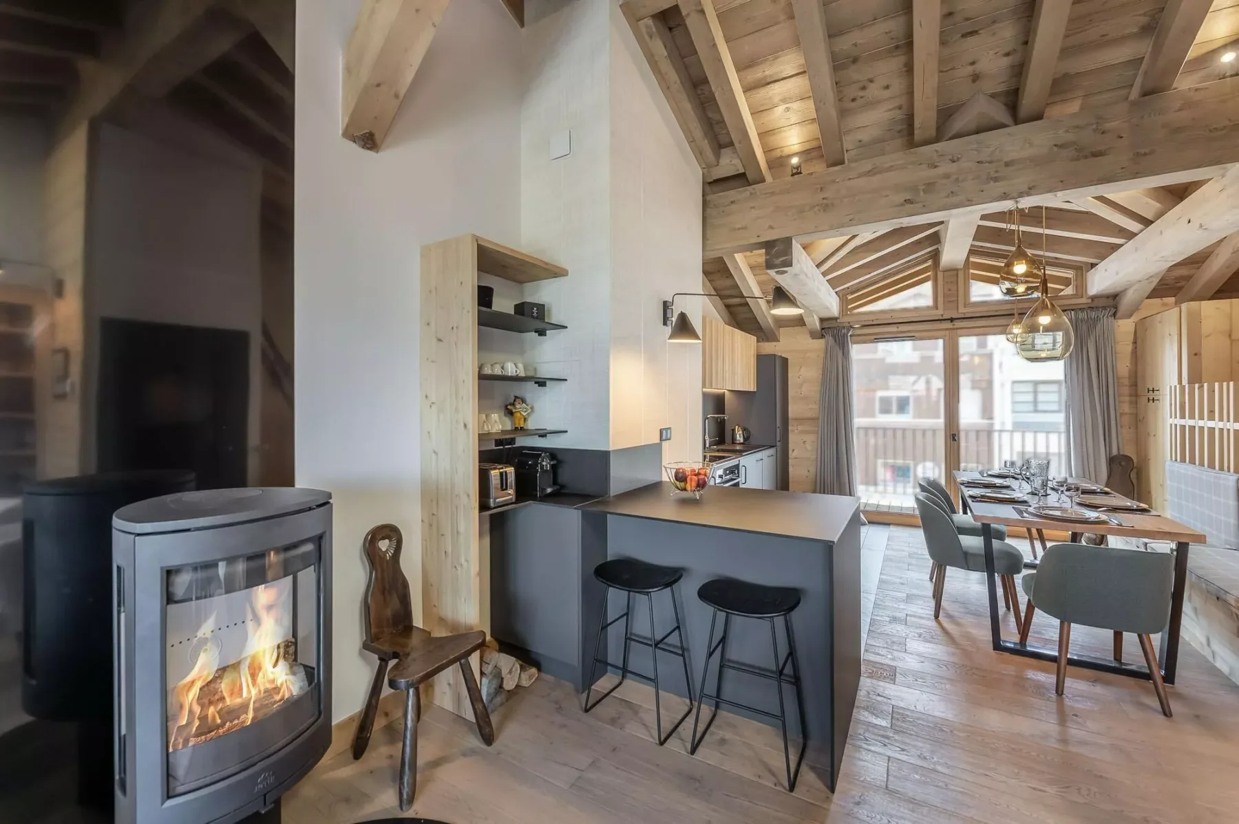 An open-plan kitchen and dining area with a counter, stools, and a wood-beamed ceiling.