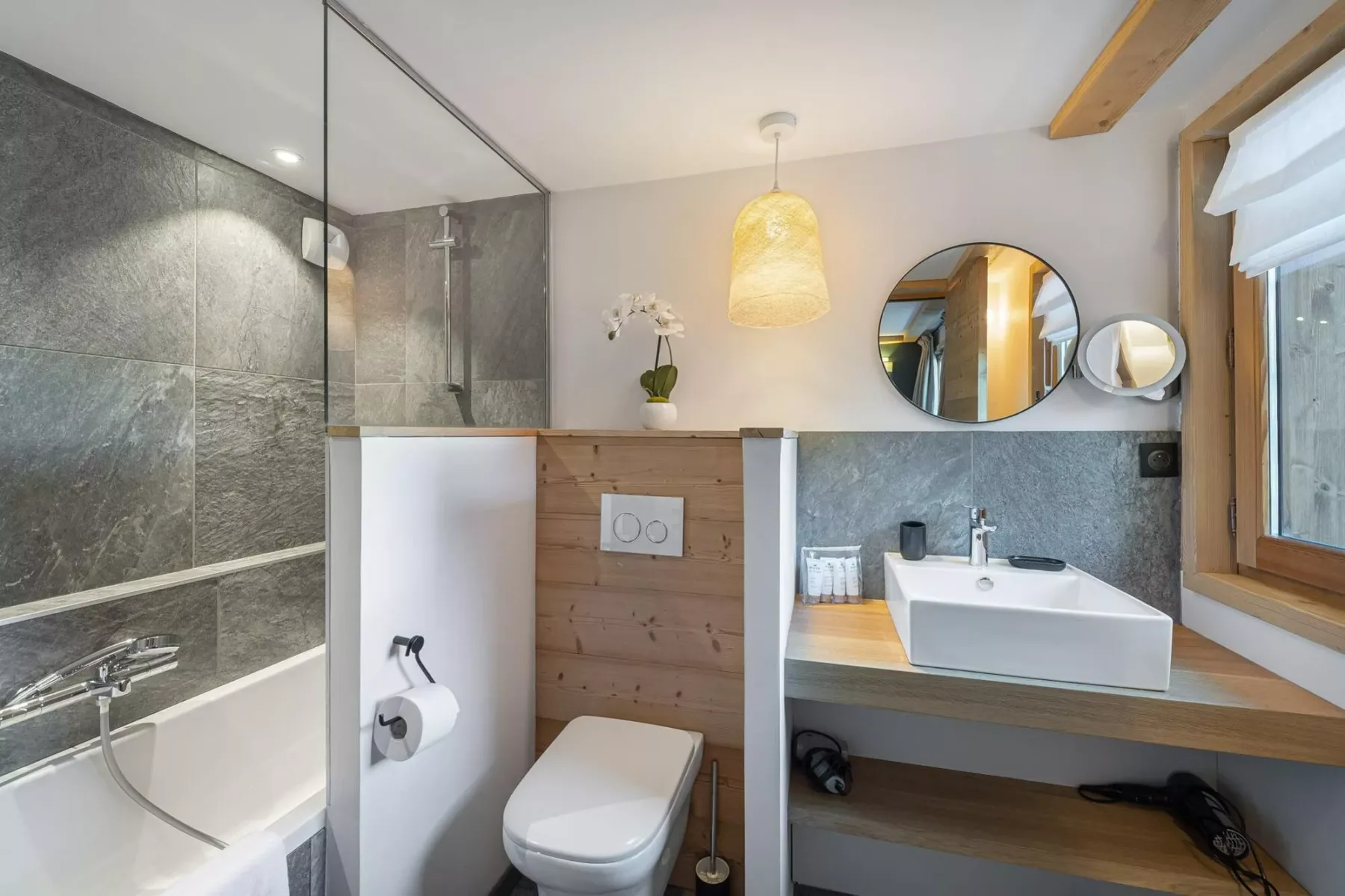 A modern bathroom with a bathtub, toilet, and sink beneath a wall mirror.