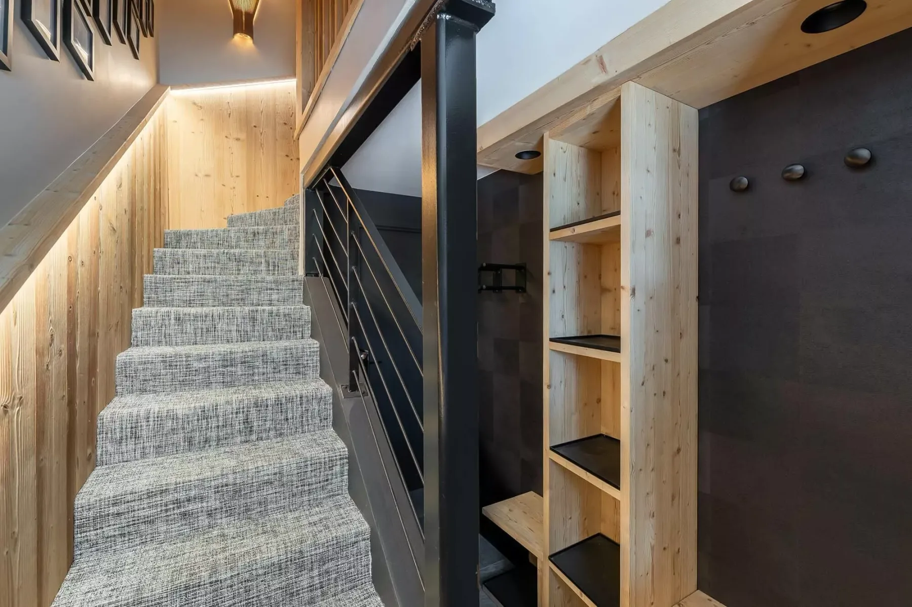 A carpeted staircase rises beside pale wood shelving and dark walls.
