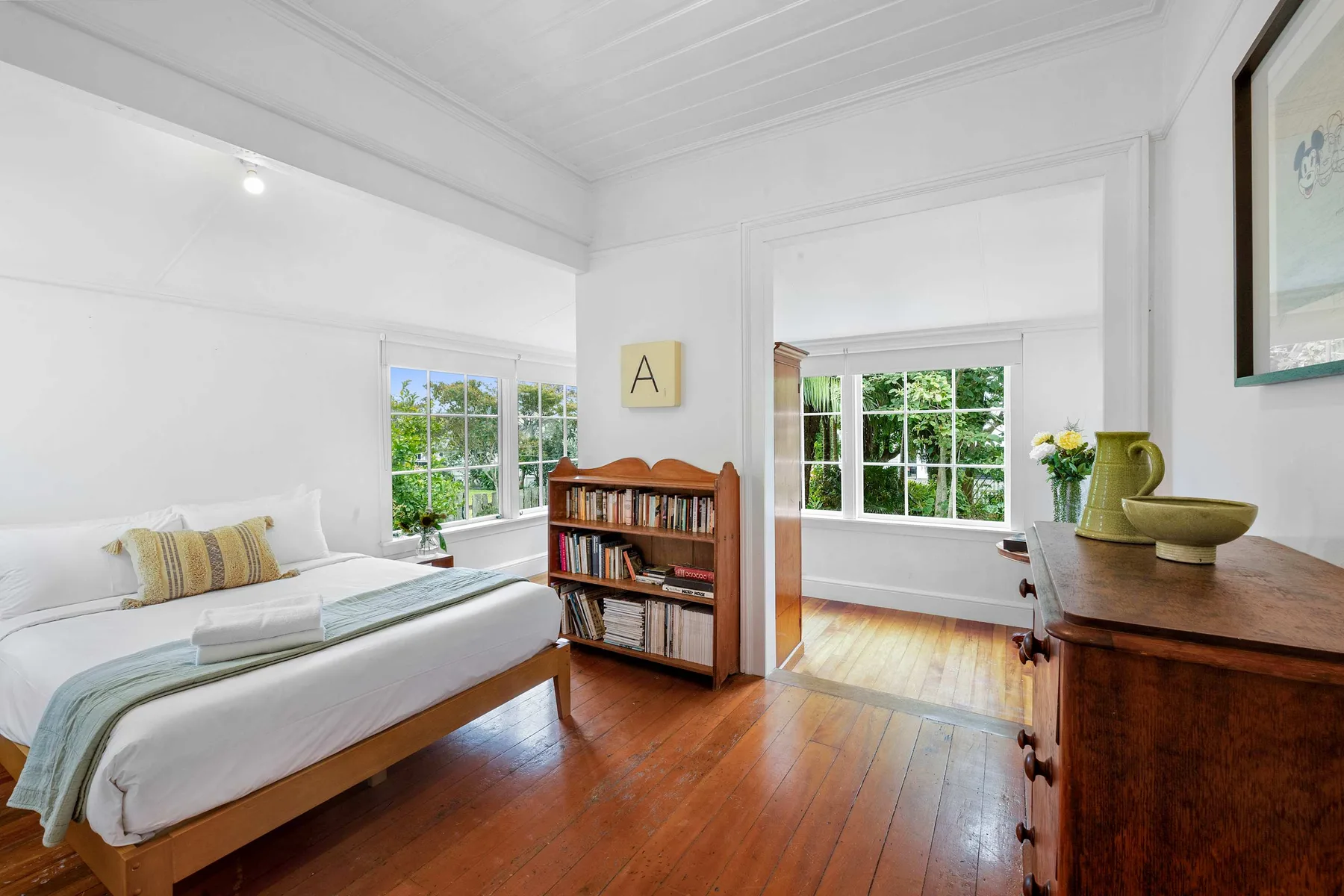 Un dormitorio luminoso se abre a una sala de estar con grandes ventanas y suelo de madera.