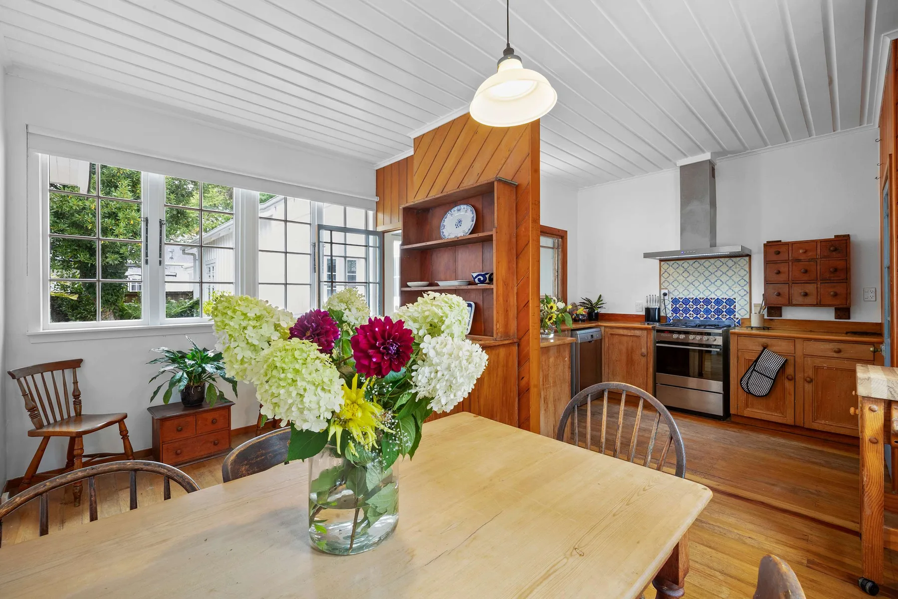 Una cocina y comedor luminosos con muebles de madera y flores sobre la mesa.