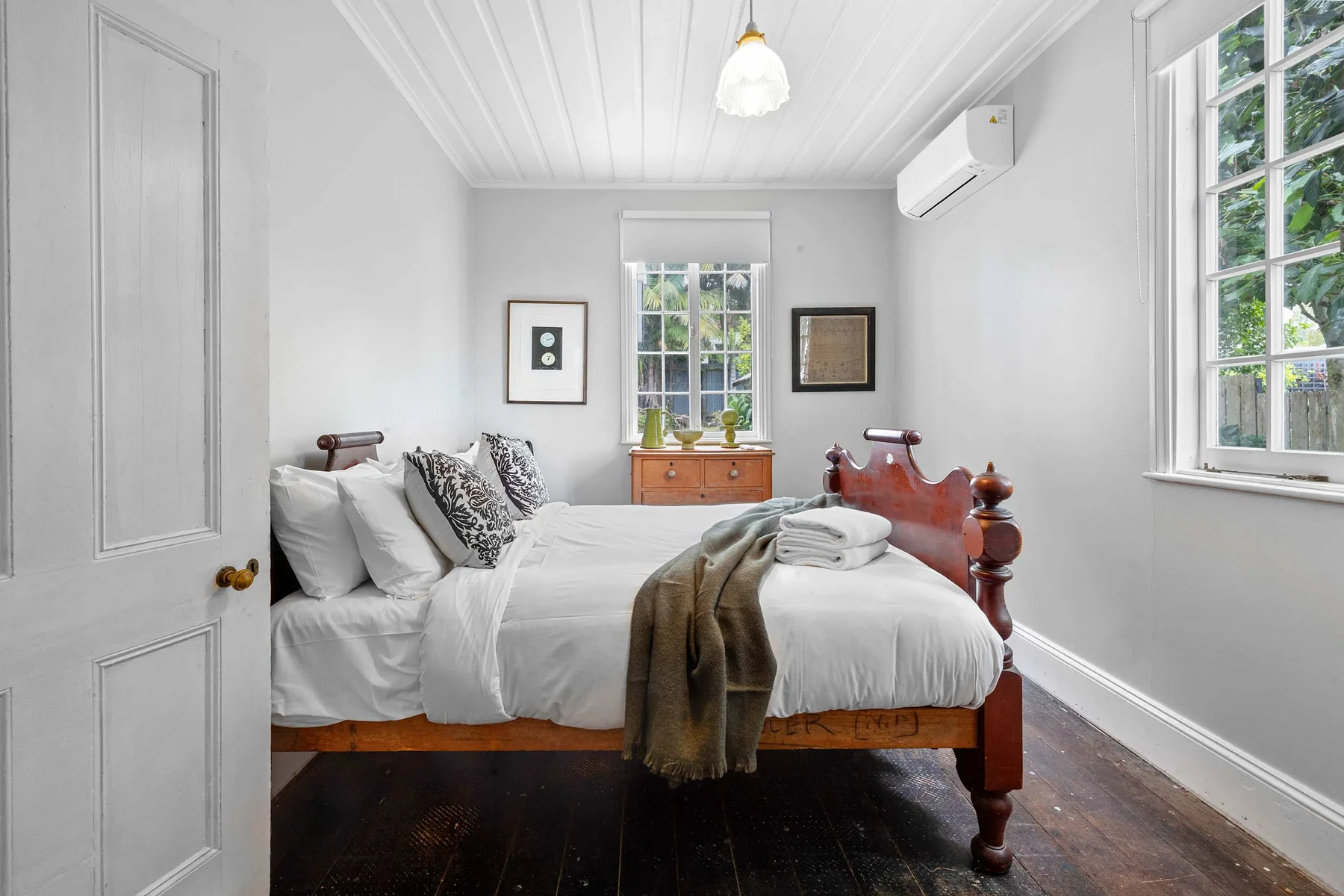 Un dormitorio luminoso con una cama blanca y ventanas altas.