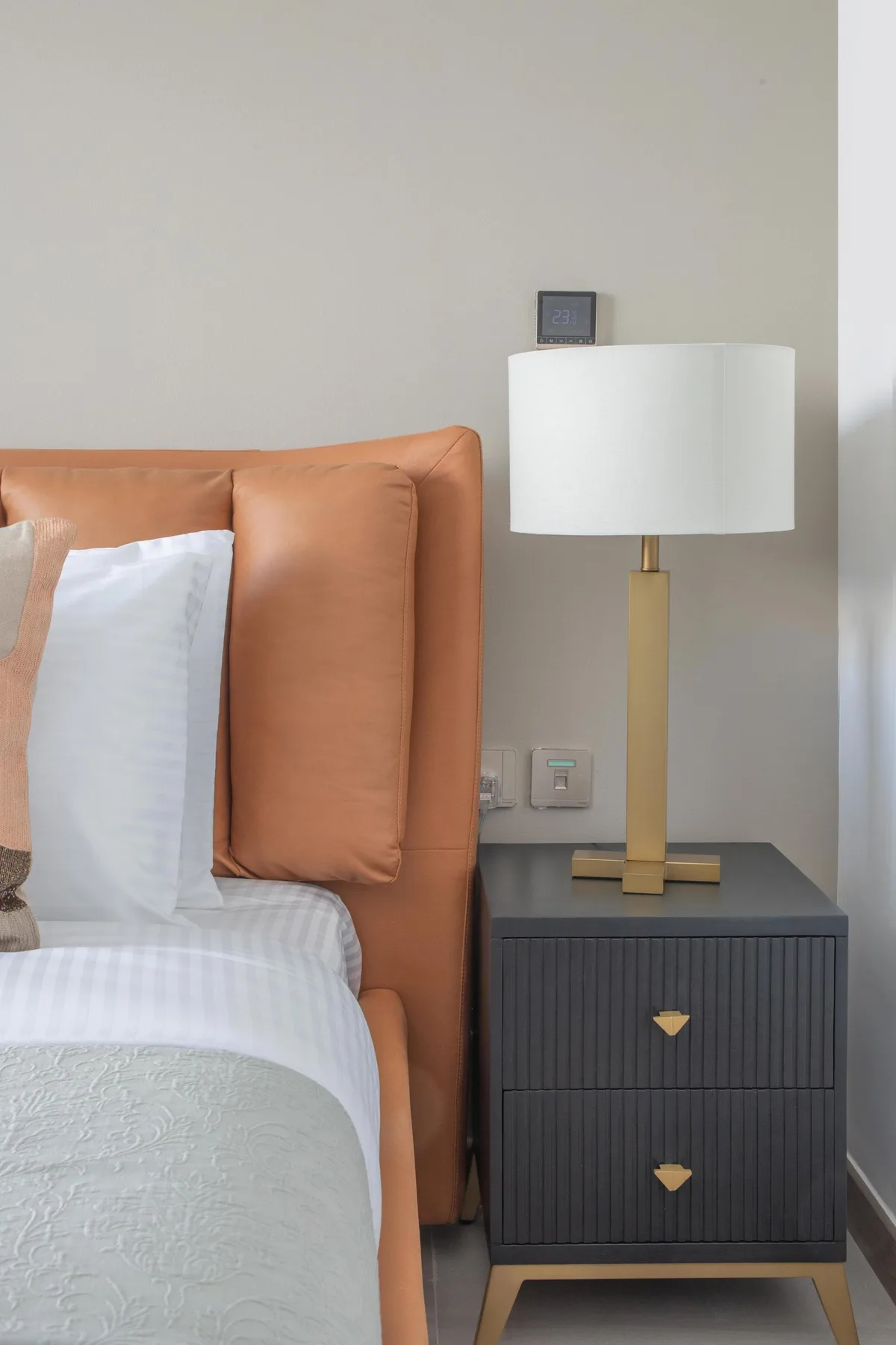A bedroom scene with a bed beside a dark bedside table and lamp.