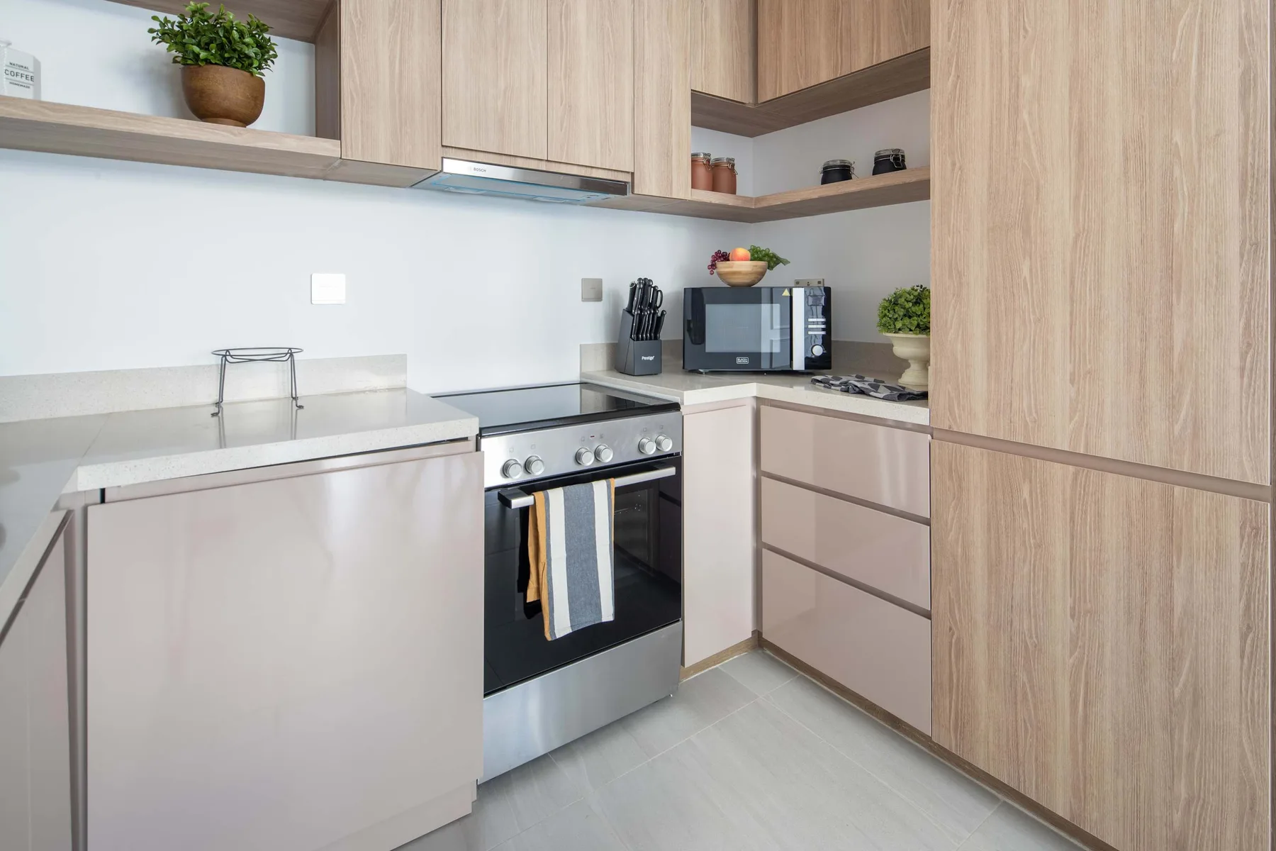 A modern kitchen with light wood cabinetry, a cooktop, and countertop appliances.