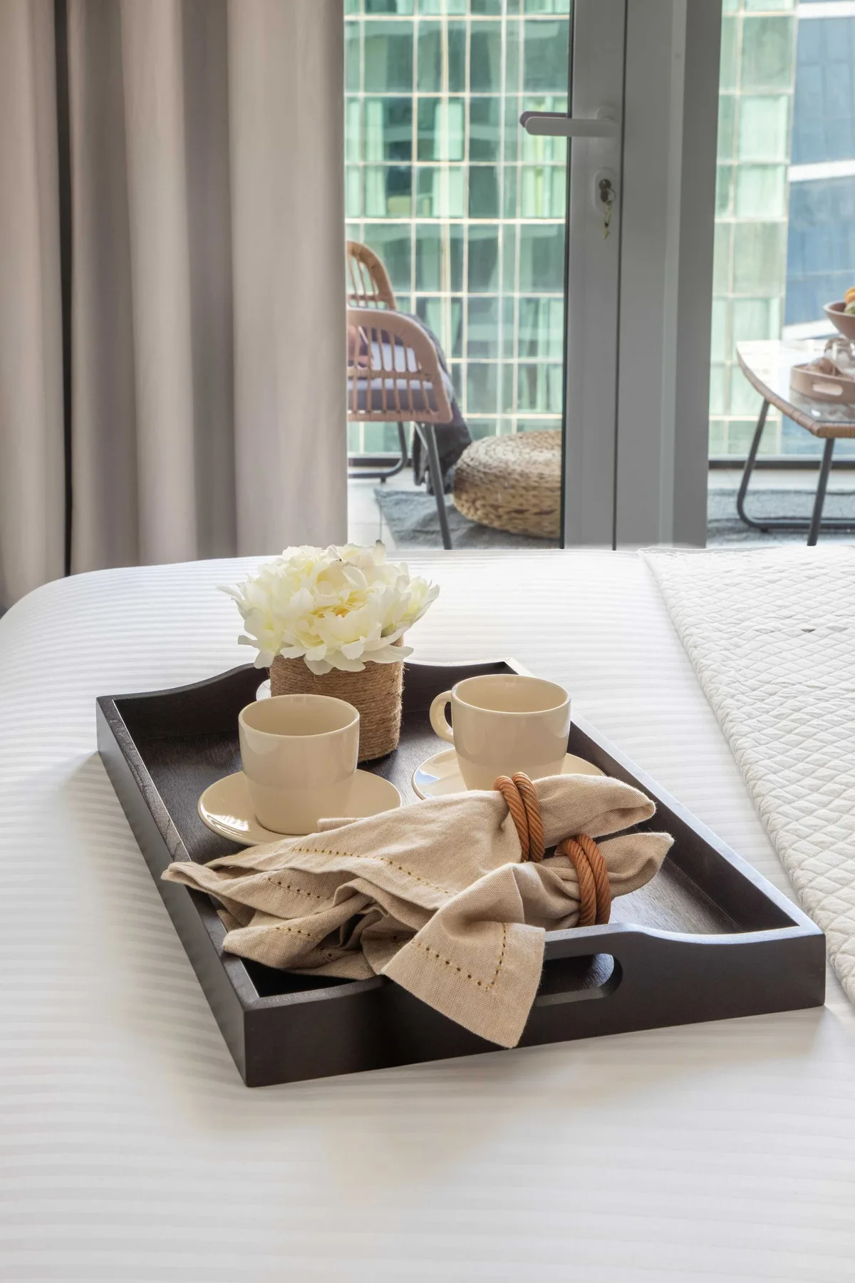 A bedroom with a tray of cups and flowers on the bed beside glass doors.