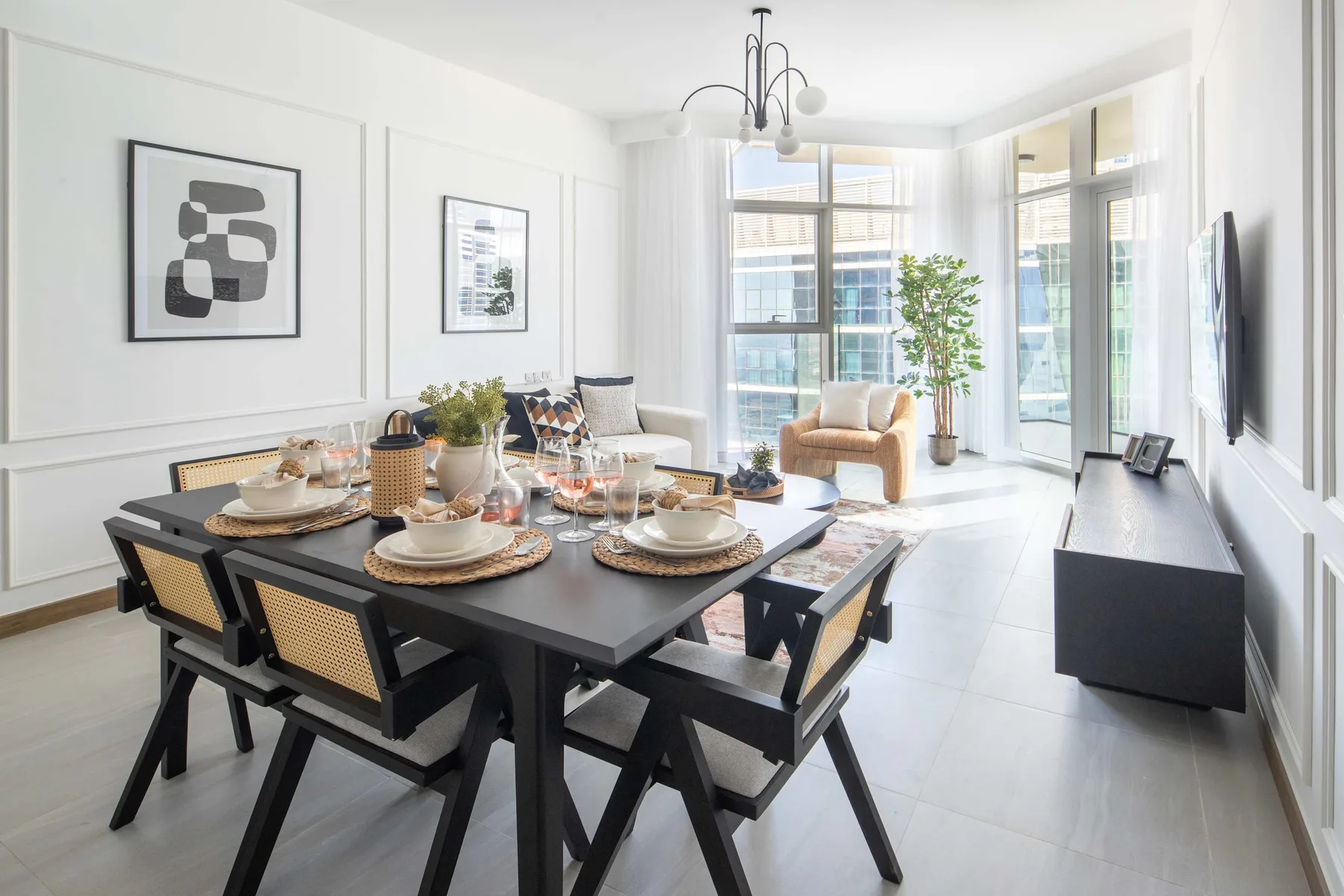 A bright dining and living area has a set table and large windows.
