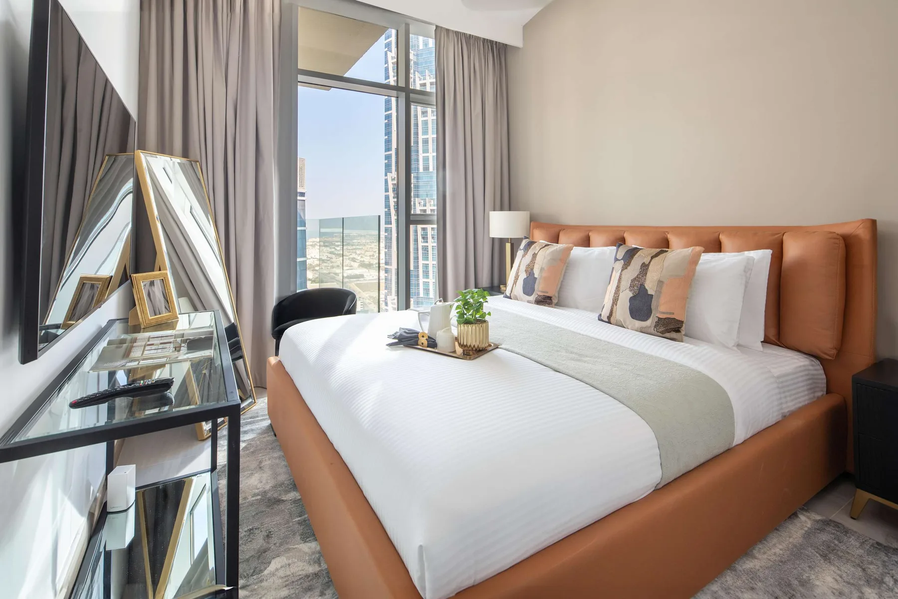 A bedroom with a neatly made bed, bedside lamp, and tall windows.