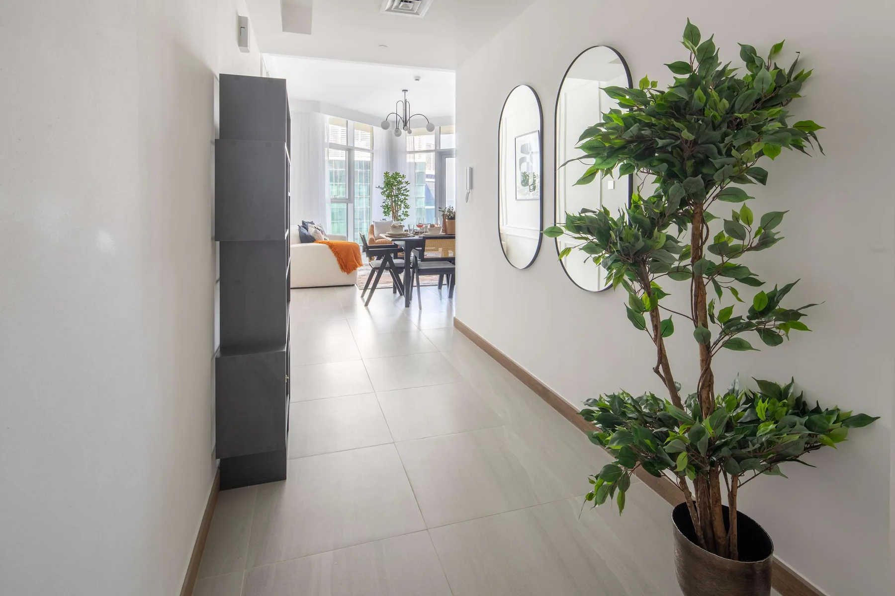 A bright hallway opens into a dining area, with a leafy plant beside the wall.