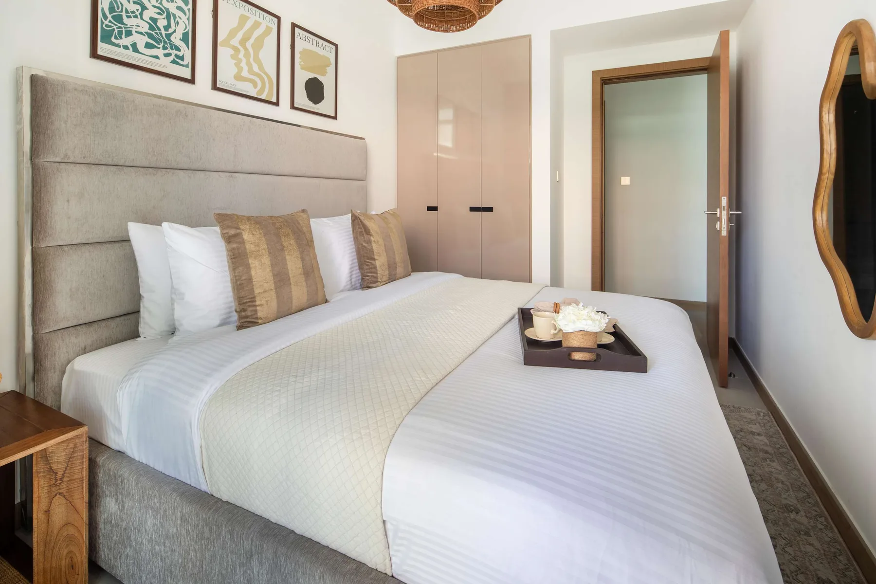 A bedroom with a neatly made bed, framed artwork, and a wardrobe.