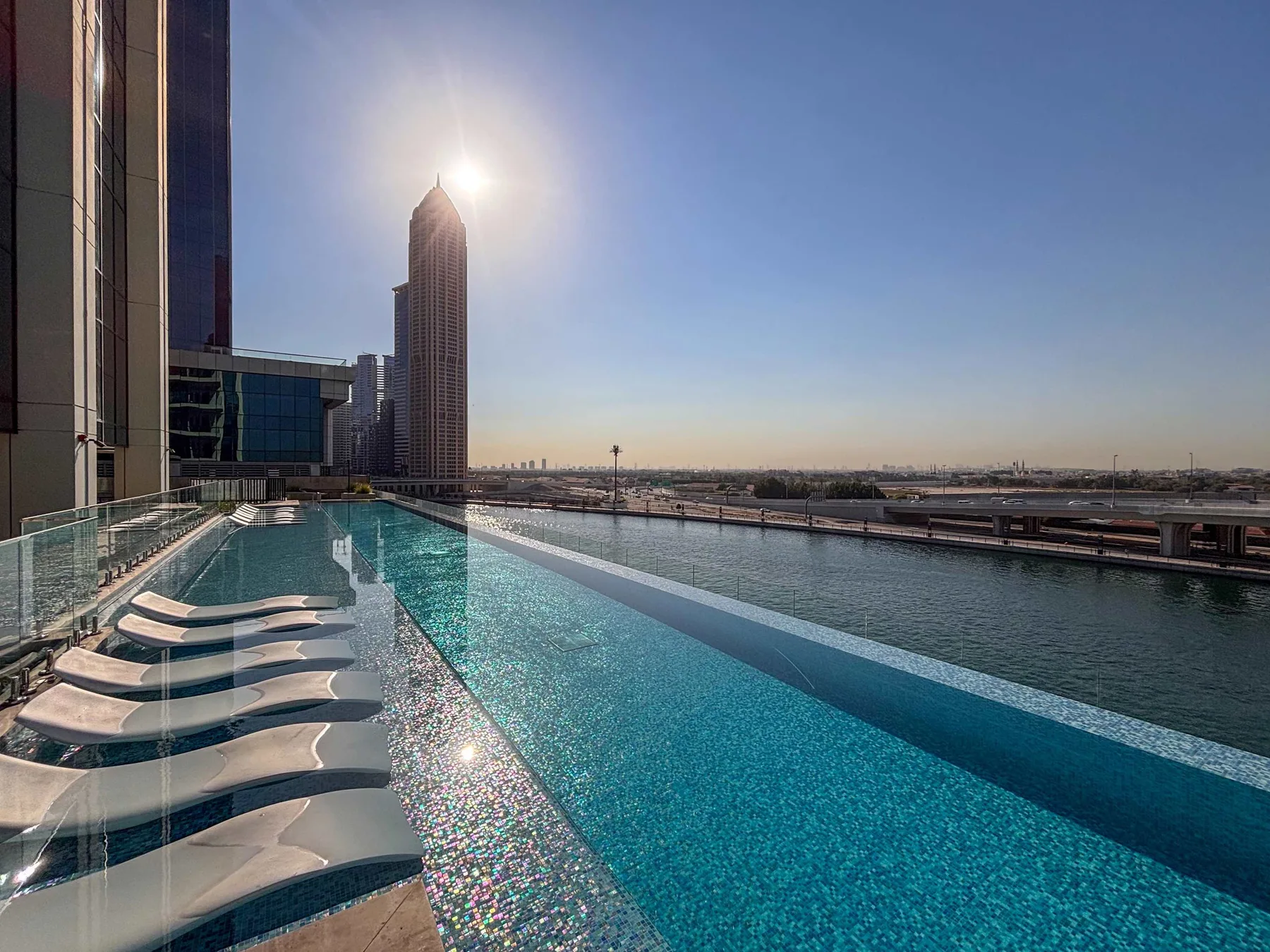 A rooftop swimming pool with lounge chairs overlooks nearby buildings and the city skyline.