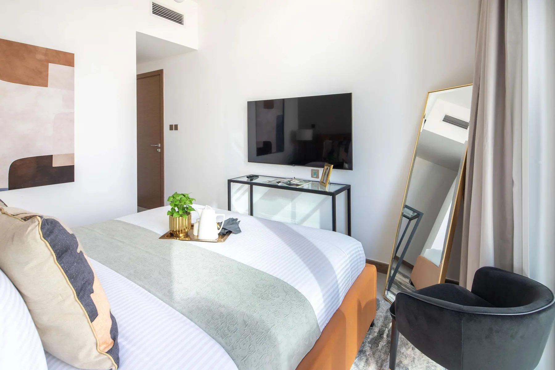 A bright bedroom with a neatly made bed and a television on the wall.