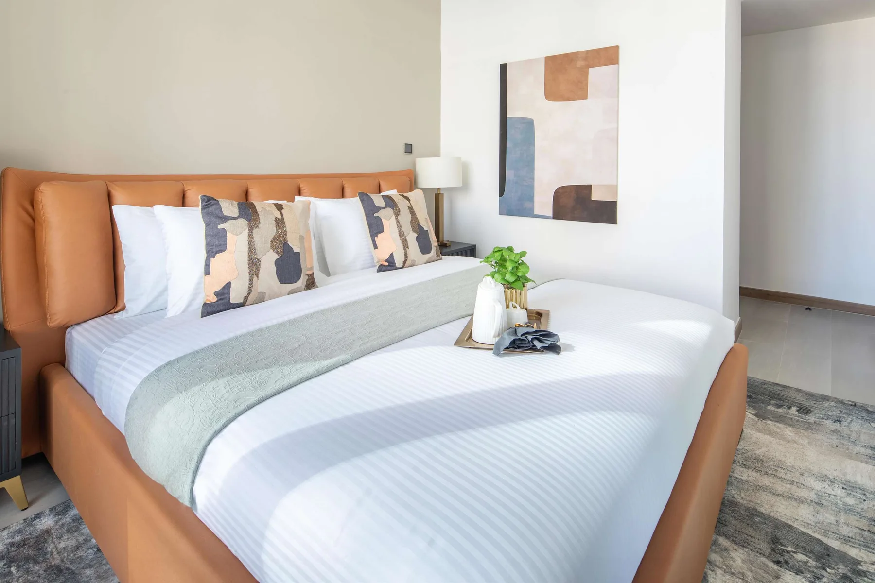 A bedroom with a neatly made bed, decorative pillows, and abstract wall art.