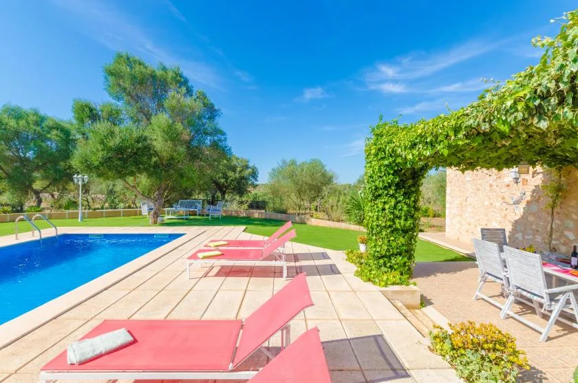 Zona de piscina exterior con tumbonas rosas y una pérgola cubierta de enredaderas.