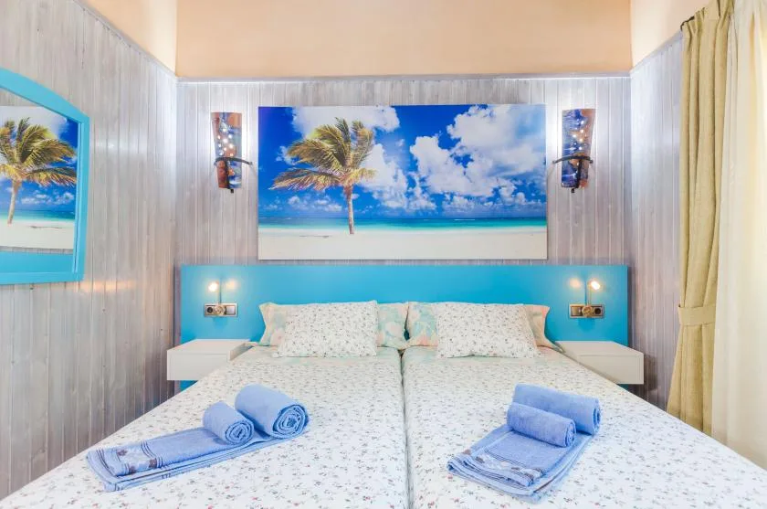 Un dormitorio con una cama bajo una gran imagen de una playa tropical.