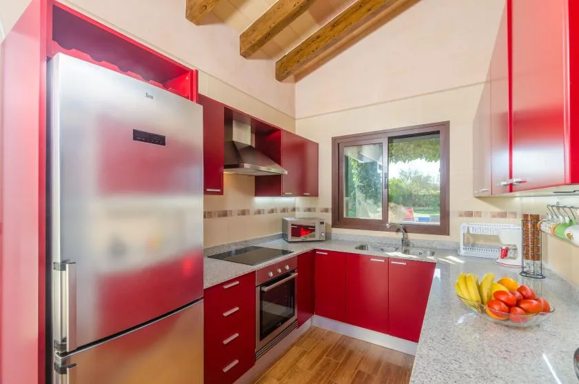 Una cocina con armarios rojos, un refrigerador y una encimera bajo vigas de madera.