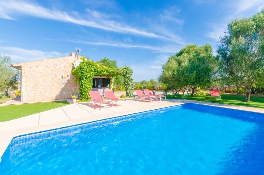Una piscina al aire libre junto a una casa de piedra, con tumbonas en el patio.