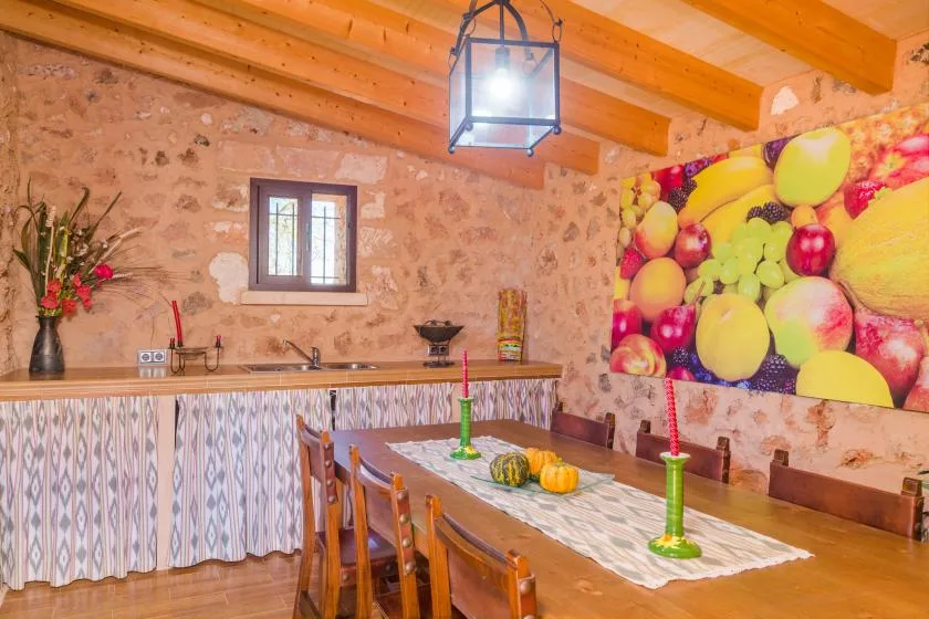 Un comedor rústico con una mesa larga, sillas de madera y un colorido cuadro de frutas.