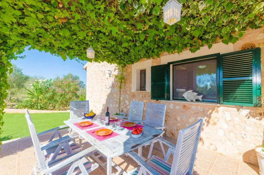 Una zona de comedor al aire libre está bajo enredaderas junto a una casa de piedra.
