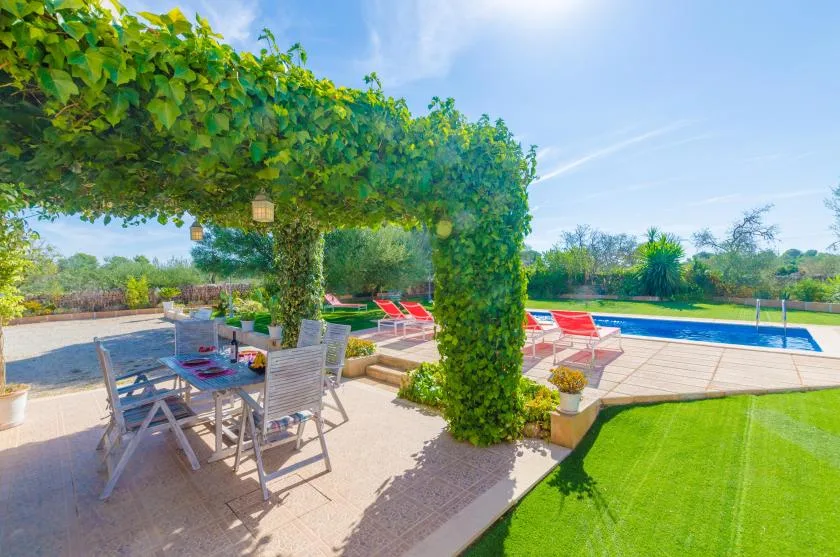 Una zona de comedor al aire libre con sombra da a una piscina y un césped verde.