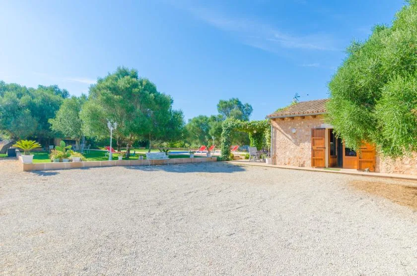 Un patio de grava junto a un edificio de piedra, rodeado de árboles y vegetación.