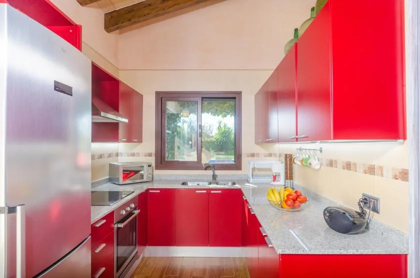 Una cocina luminosa con gabinetes rojos, una encimera y una ventana con vistas a la vegetación.