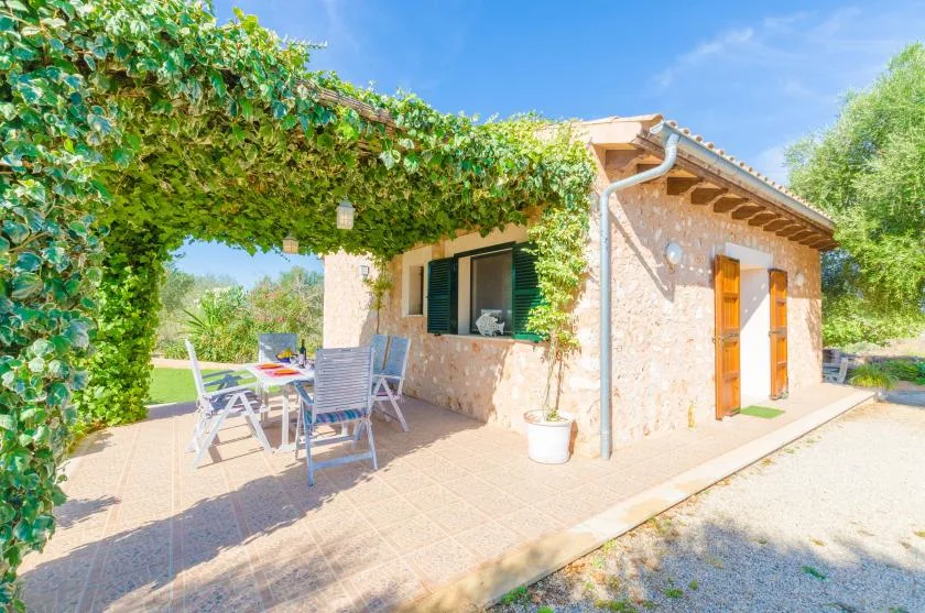 Una casa de piedra tiene un patio sombreado con asientos al aire libre y enredaderas.