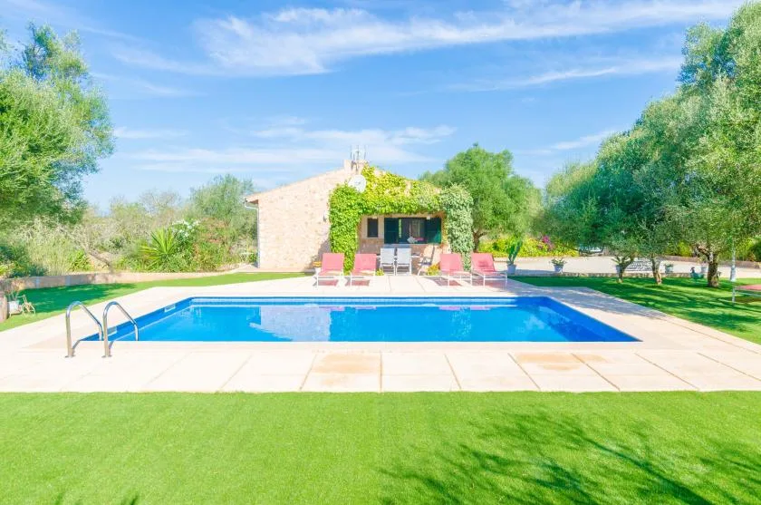 Una piscina al aire libre está junto a un césped, árboles y un pequeño edificio de piedra.