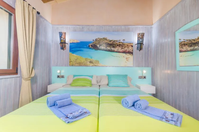 Un dormitorio con dos camas vestidas con ropa de cama verde y azul bajo un cuadro de paisaje costero.