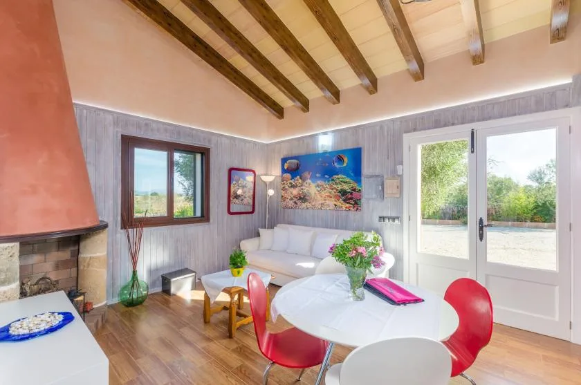 Un salón luminoso con asientos blancos, una mesa redonda y puertas que dan a un jardín.