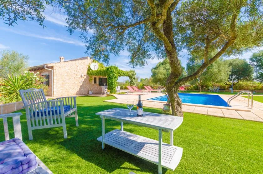 Un patio ajardinado con piscina, asientos al aire libre y una casa de piedra.