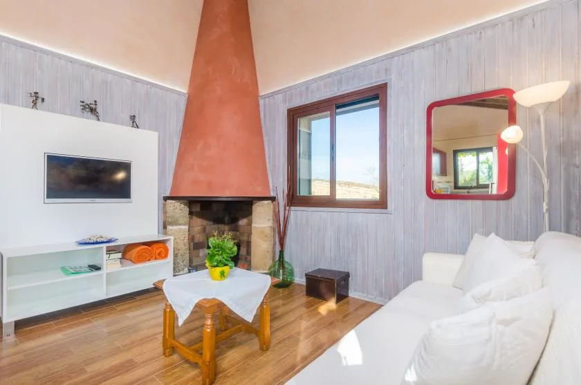 Una sala de estar con chimenea, asientos blancos y una mesa pequeña.