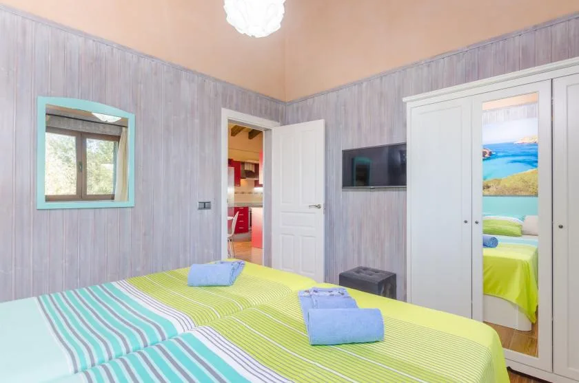 Un dormitorio luminoso con ropa de cama a rayas, un televisor en la pared y puertas abiertas.