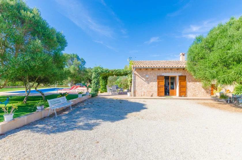 Un edificio de piedra da a un patio de grava, con árboles y una piscina cerca.