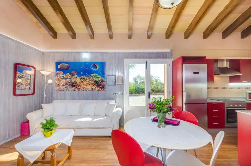 Una zona de estar y comedor con asientos blancos, una mesa y gabinetes de cocina rojos.