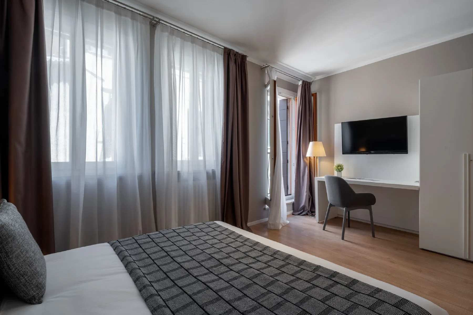 A bedroom with a bed beside a desk and television.