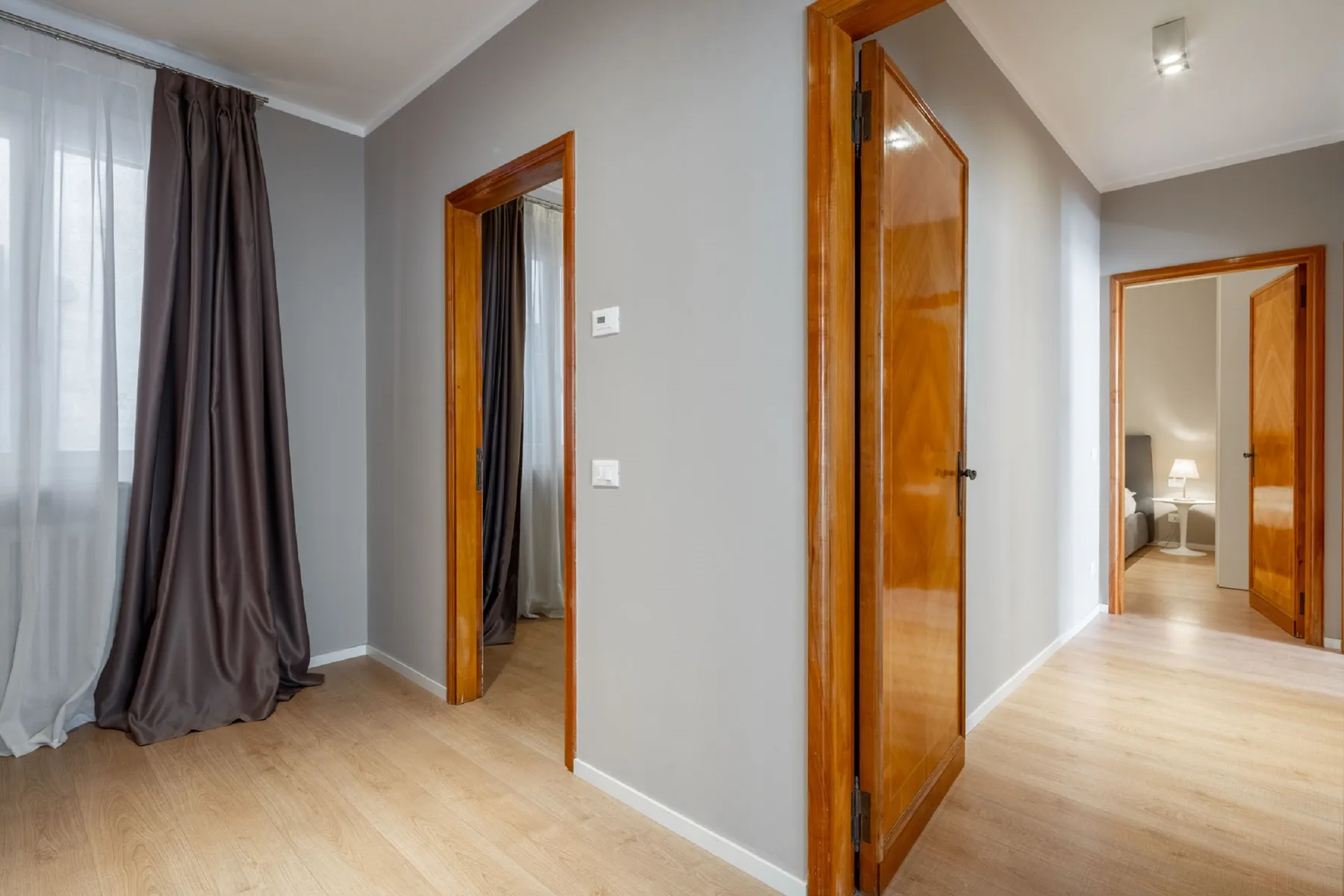 A bright hallway with wooden doors and a view into an adjoining room.