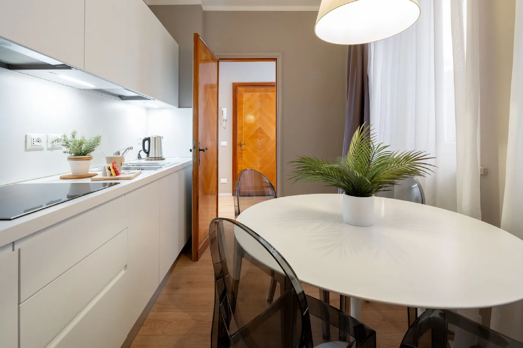 A modern kitchen and dining area with a white table and potted plant.