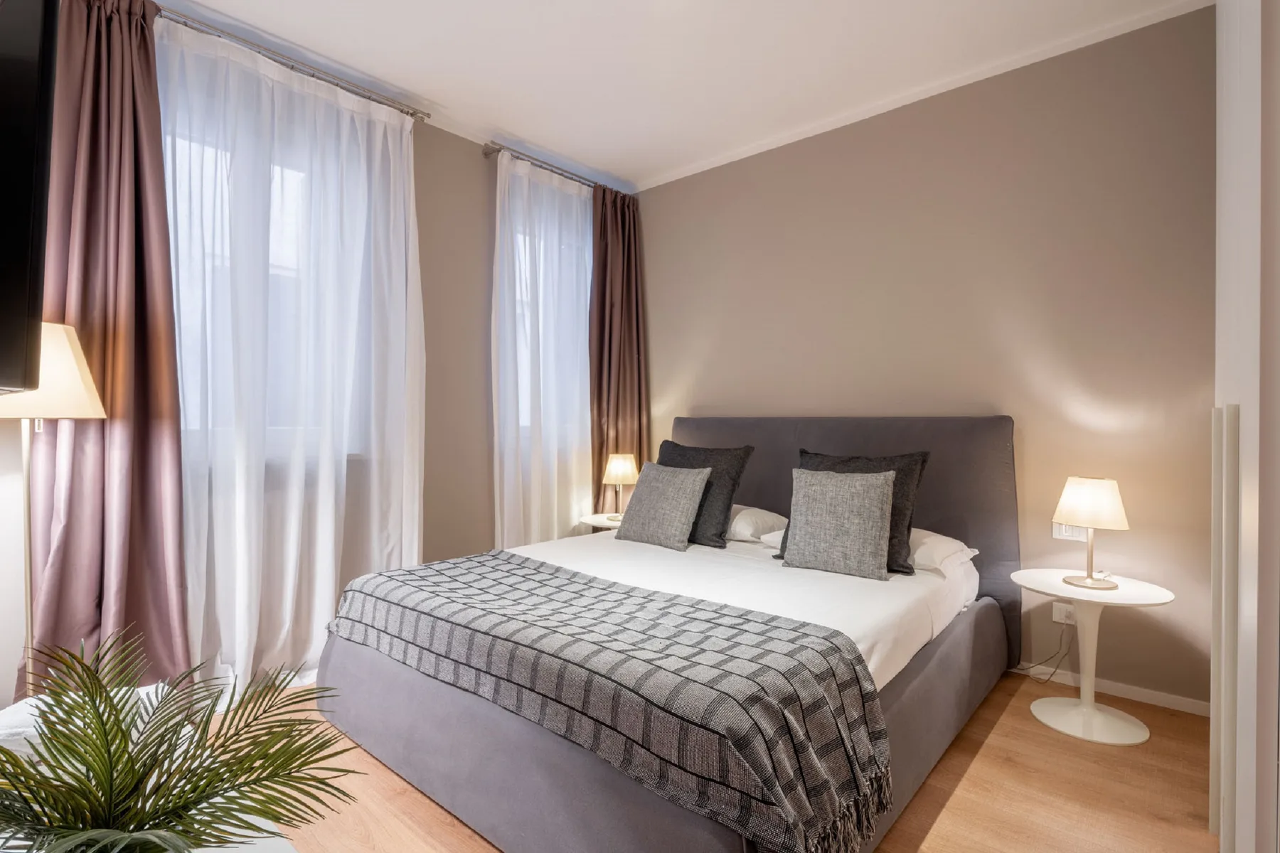 A bedroom with a bed dressed in white bedding and gray pillows.